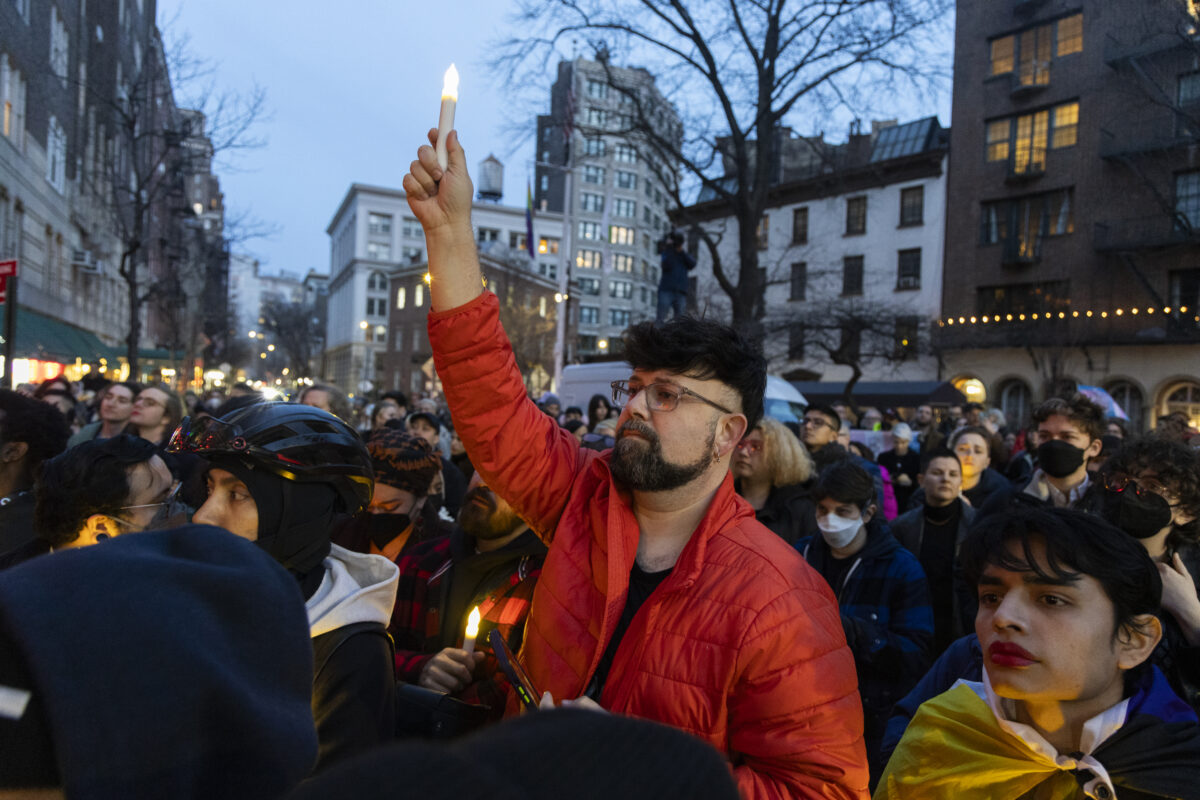 Image of a person holding a candle above a crowd of people in the street.