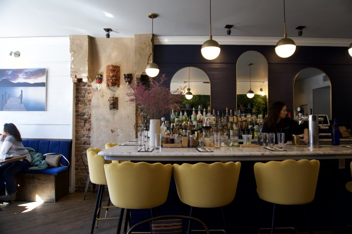 A bar with a line of yellow stools and decorative mirrors on the wall.