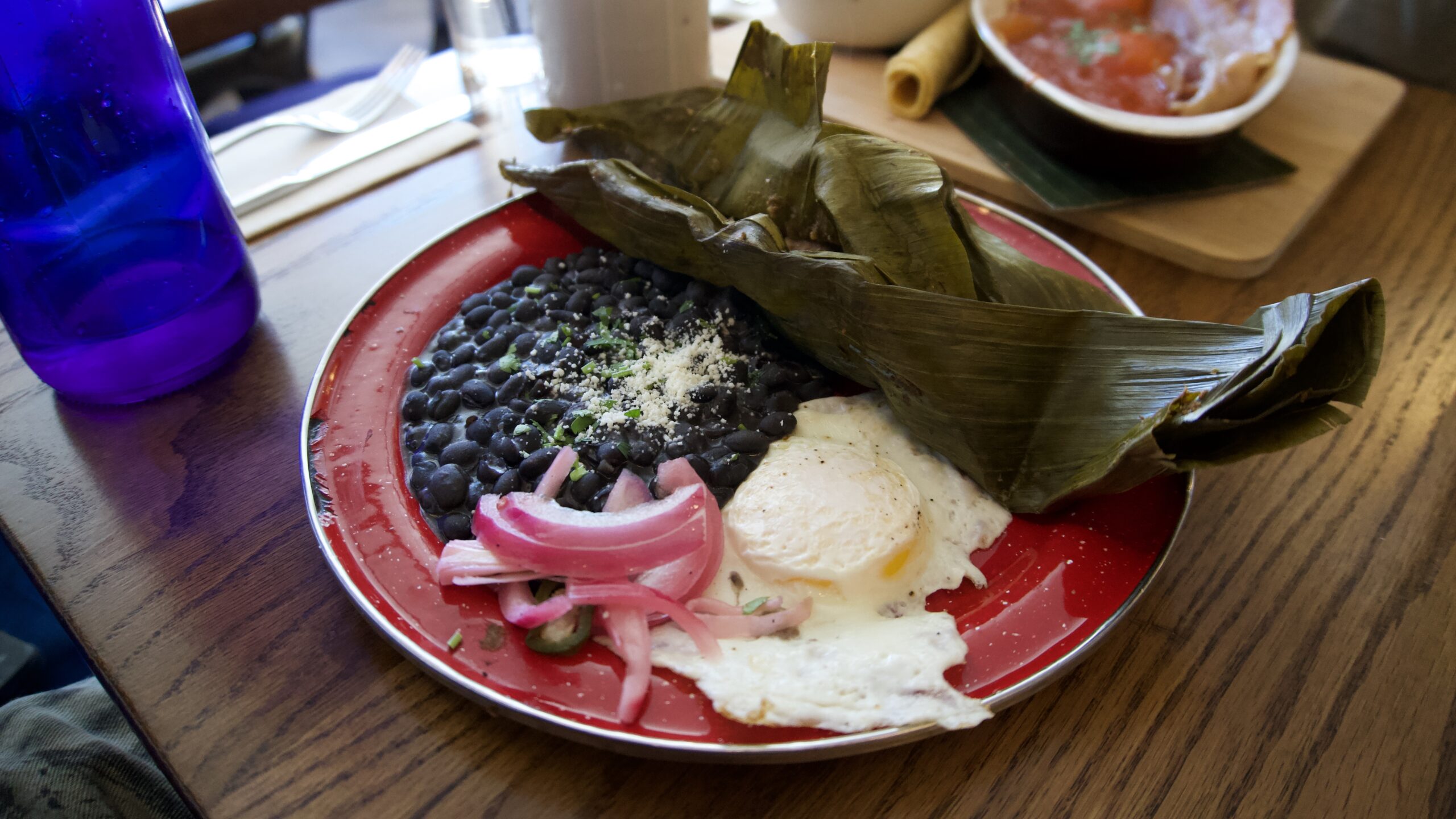A plate with beans, an egg, and a tamale wrapped in a leaf.