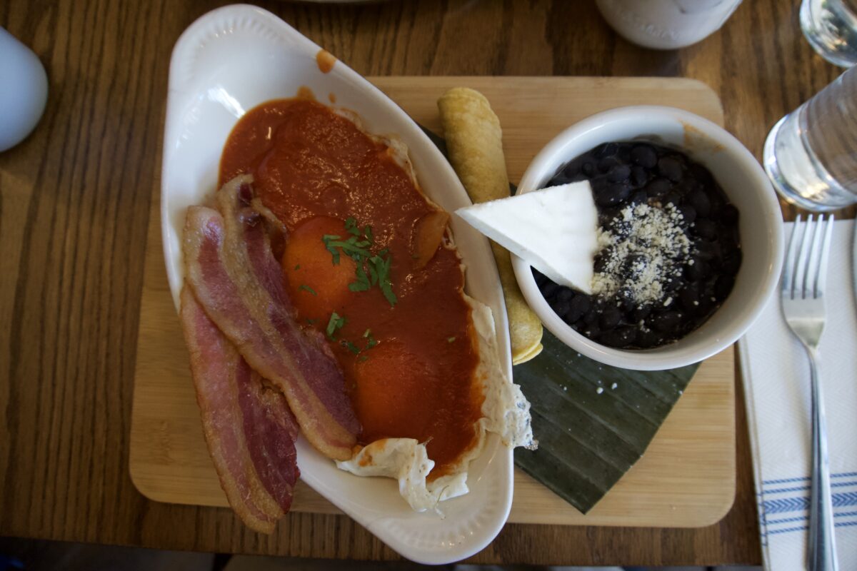 Eggs stewed in tomato salsa with bacon, beans, and tortillas in a dish.