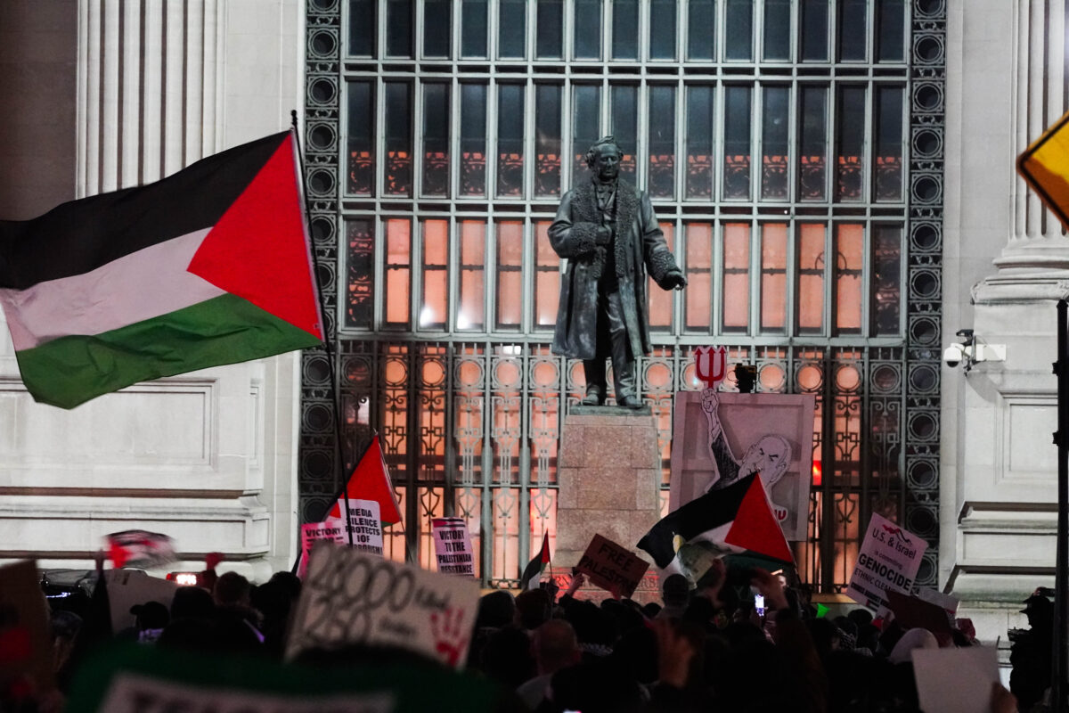 Crowd of protesters carrying large Palestinian flags and cut out of Israeli Prime Minister Netanyahu holding satan's trident surround a statue outside of Grand Central Station 