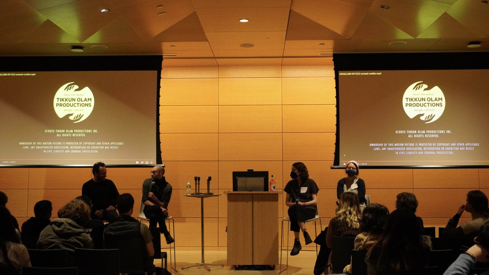 four speakers sitting on stools in front of two screens