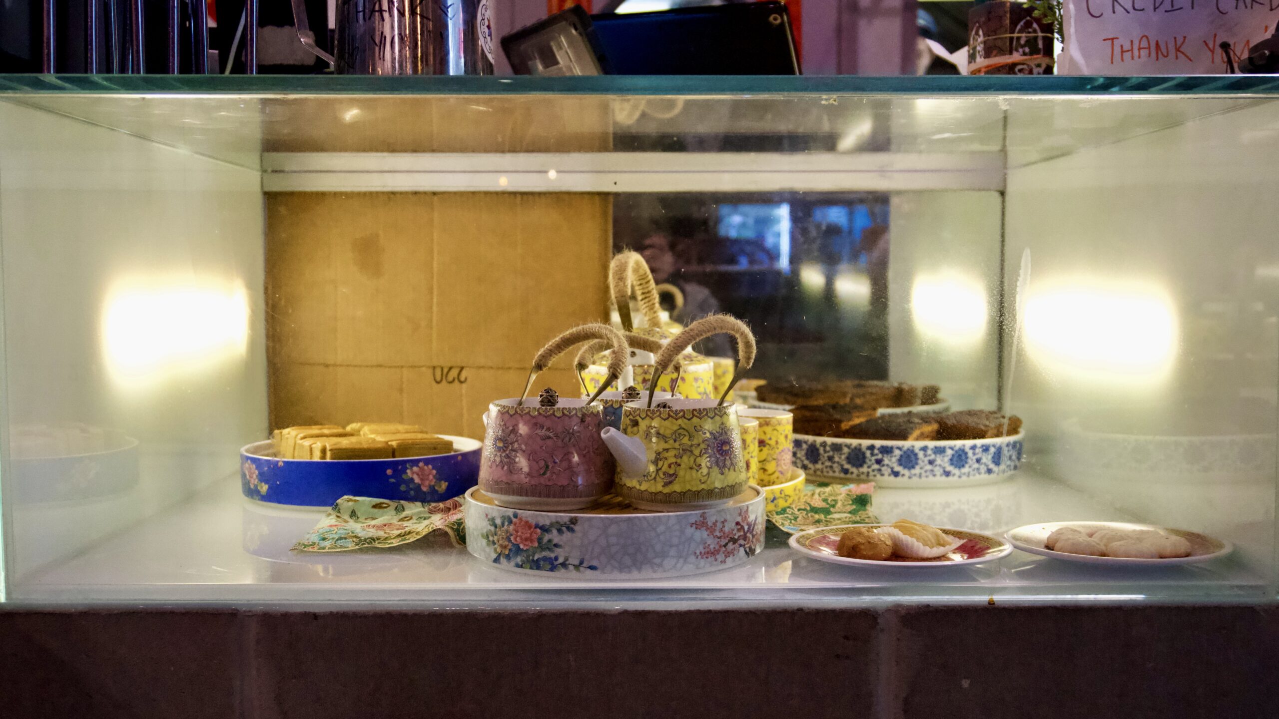Colorful teapots and cakes in patterned dishes sit in a display case.