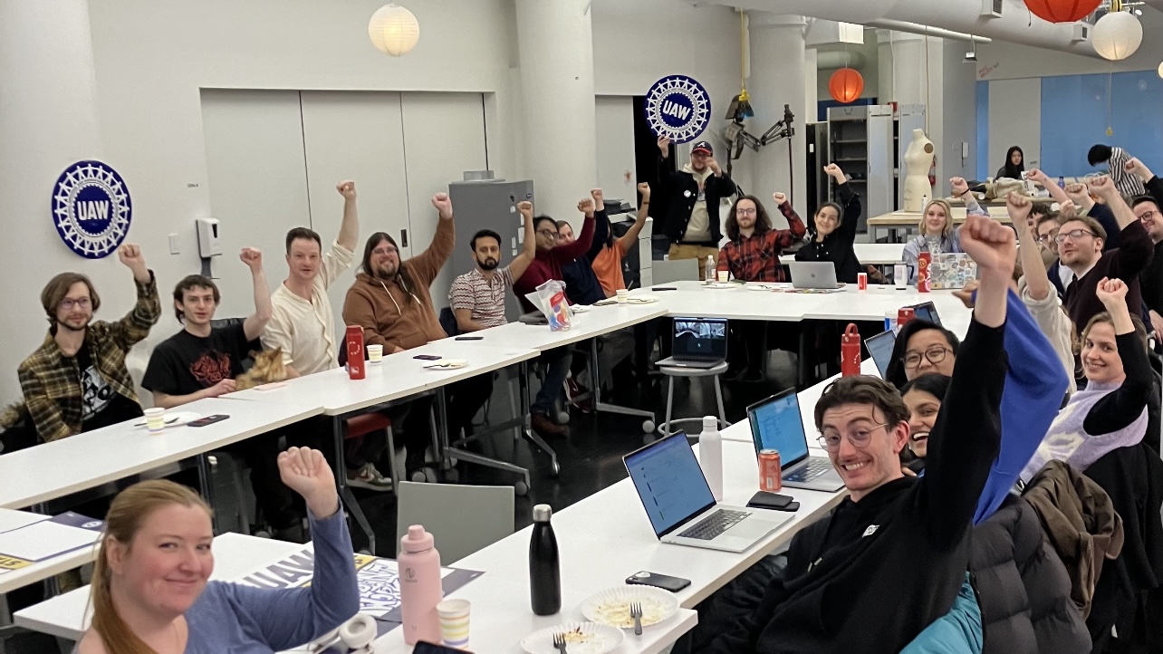 Over 20 union members with fists raised gather around a table at a recent event.