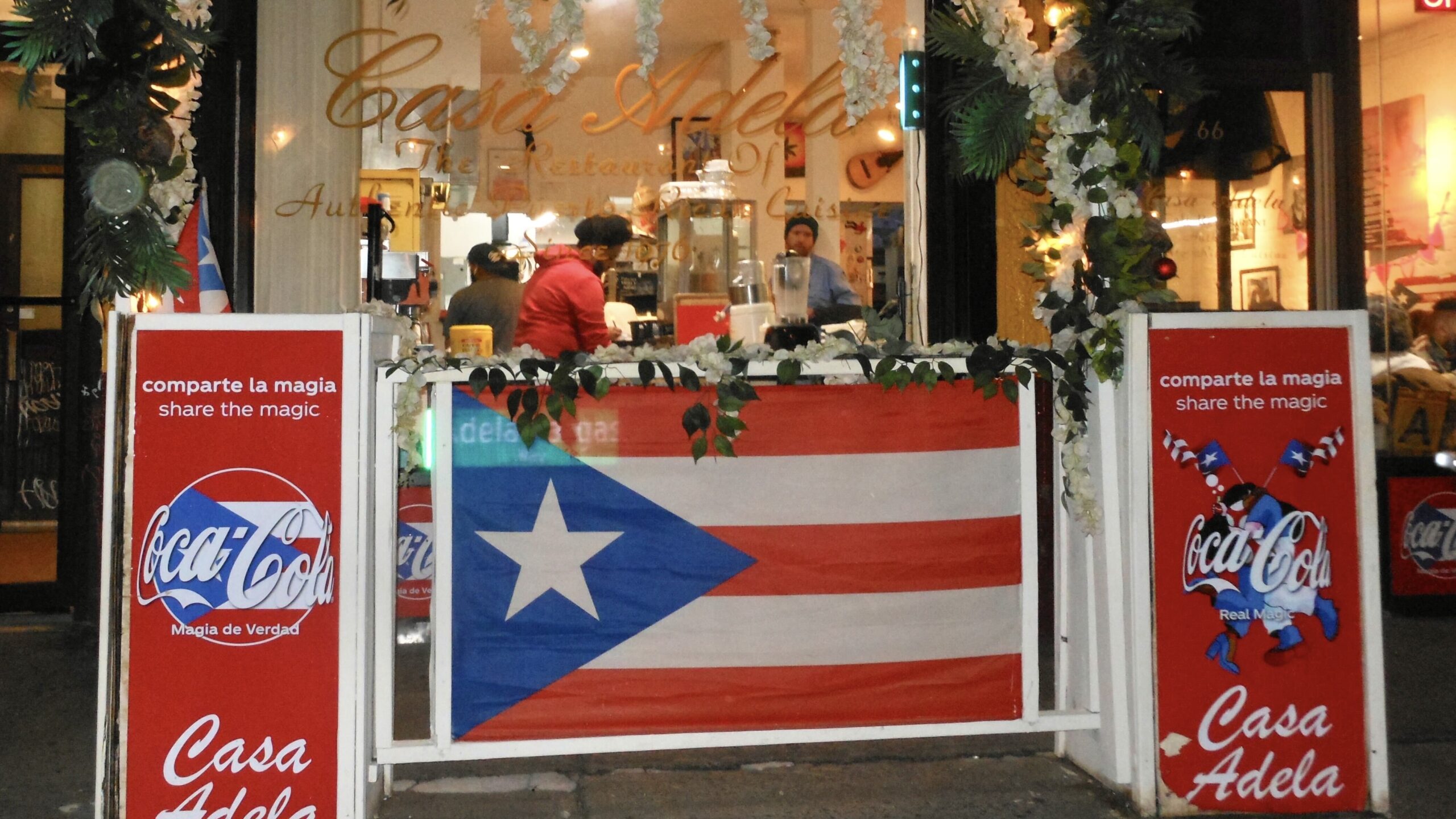 Front of restaurant with Puerto Rican flags and gold text on window reading “Casa Adela”