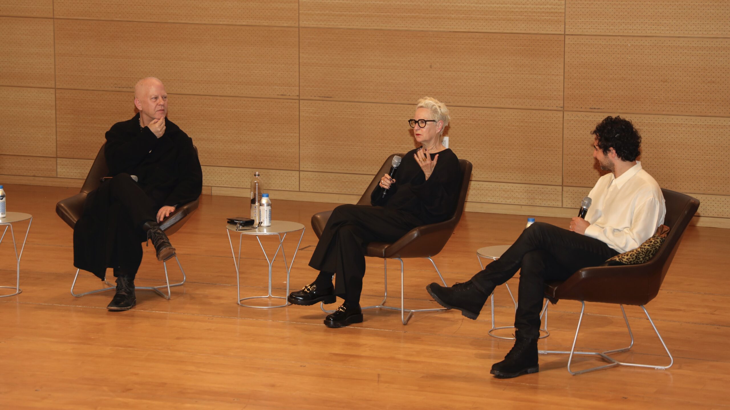 Ryan Murphy, Lou Eyrich, and Zac Posen sit side-by-side on stage in the Tishman Auditorium with microphones in their hands.