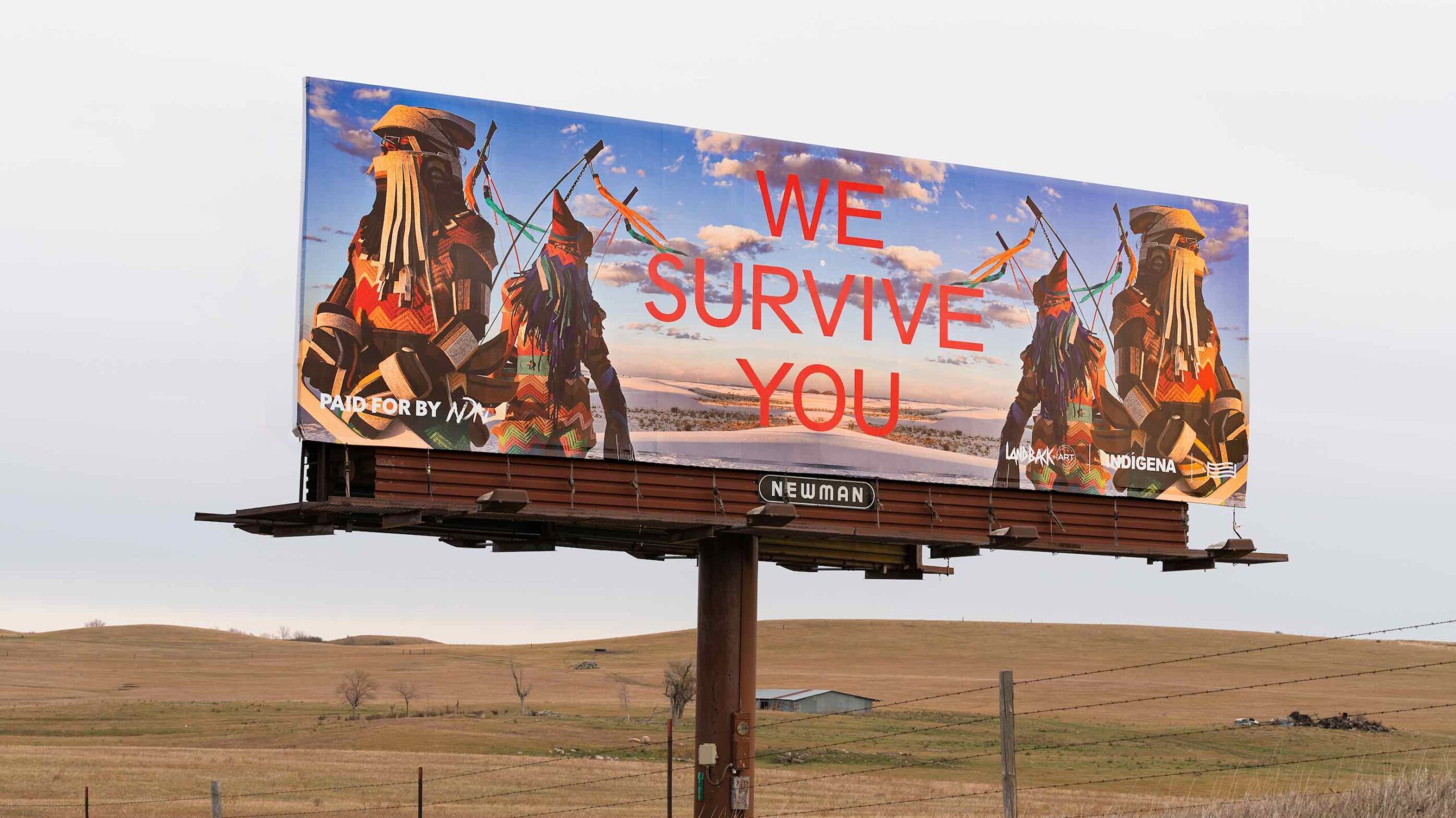 Billboard over field depicting Indigenous Peoples and red text reading "We Survive You"