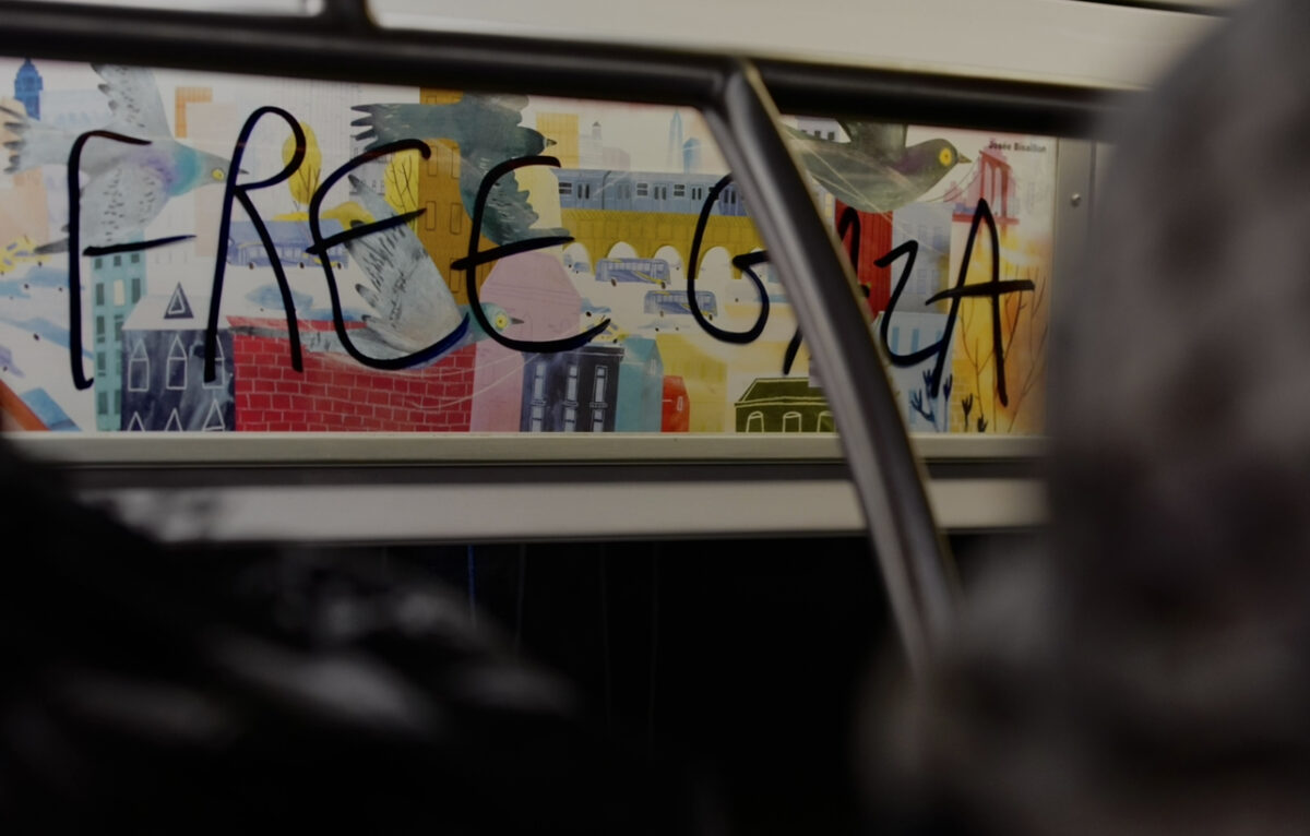  Black letters read “Free Gaza” over colorful subway advertisement 