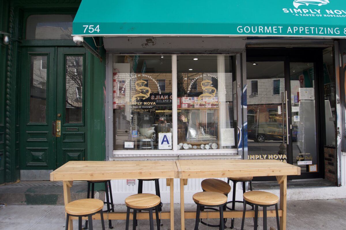 The outside of the delicatessen with a green awning and outdoor seating.