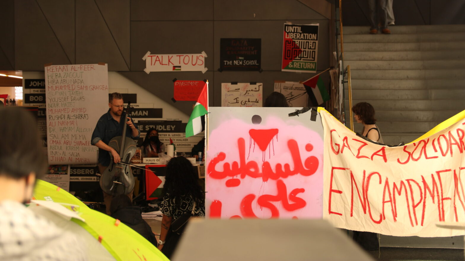 Ethan Philbrick plays cello amid Gaza Solidarity Encampment in the University Center, surrounded by protest signs