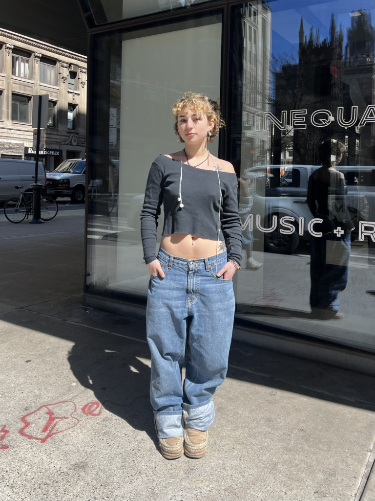 Student stands in front of The New School University Center wearing a gray long sleeve t-shirt, baggy blue jeans, and brown platform Ugg boots.