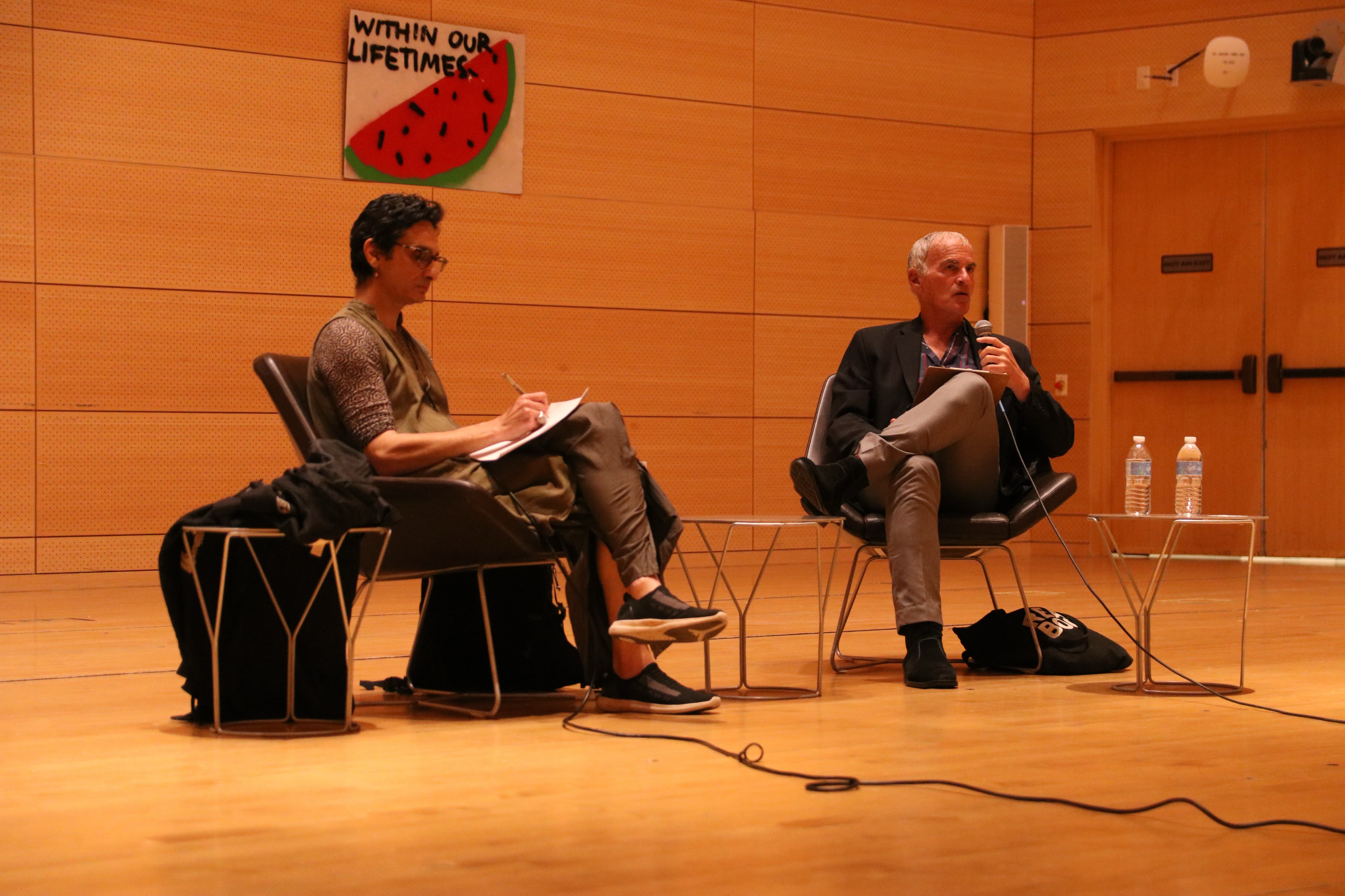 Abou Farman and Norman Finkelstein seated on chairs on the stage at Tishman Auditorium in the University Center.