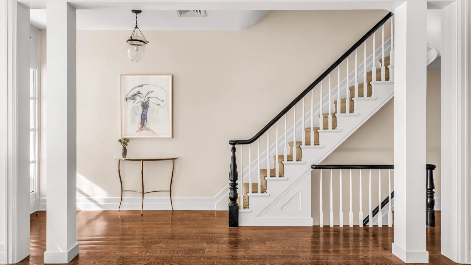 Alt text: Entryway to townhouse –beige wall with white trimming, abstract painting to the left of the frame and staircase to the right