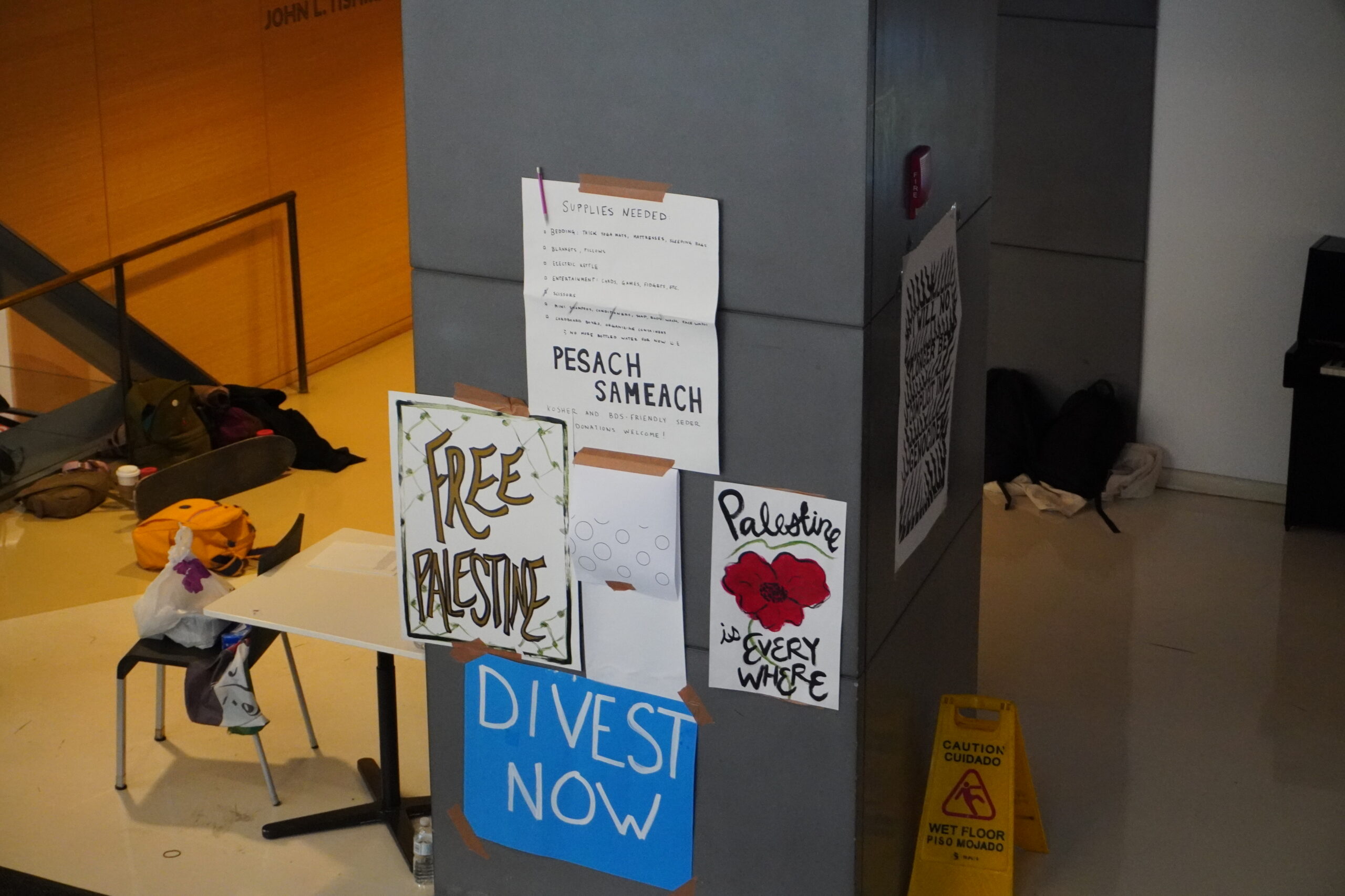 Photo of a pole with posters. one poster reads "divest now"