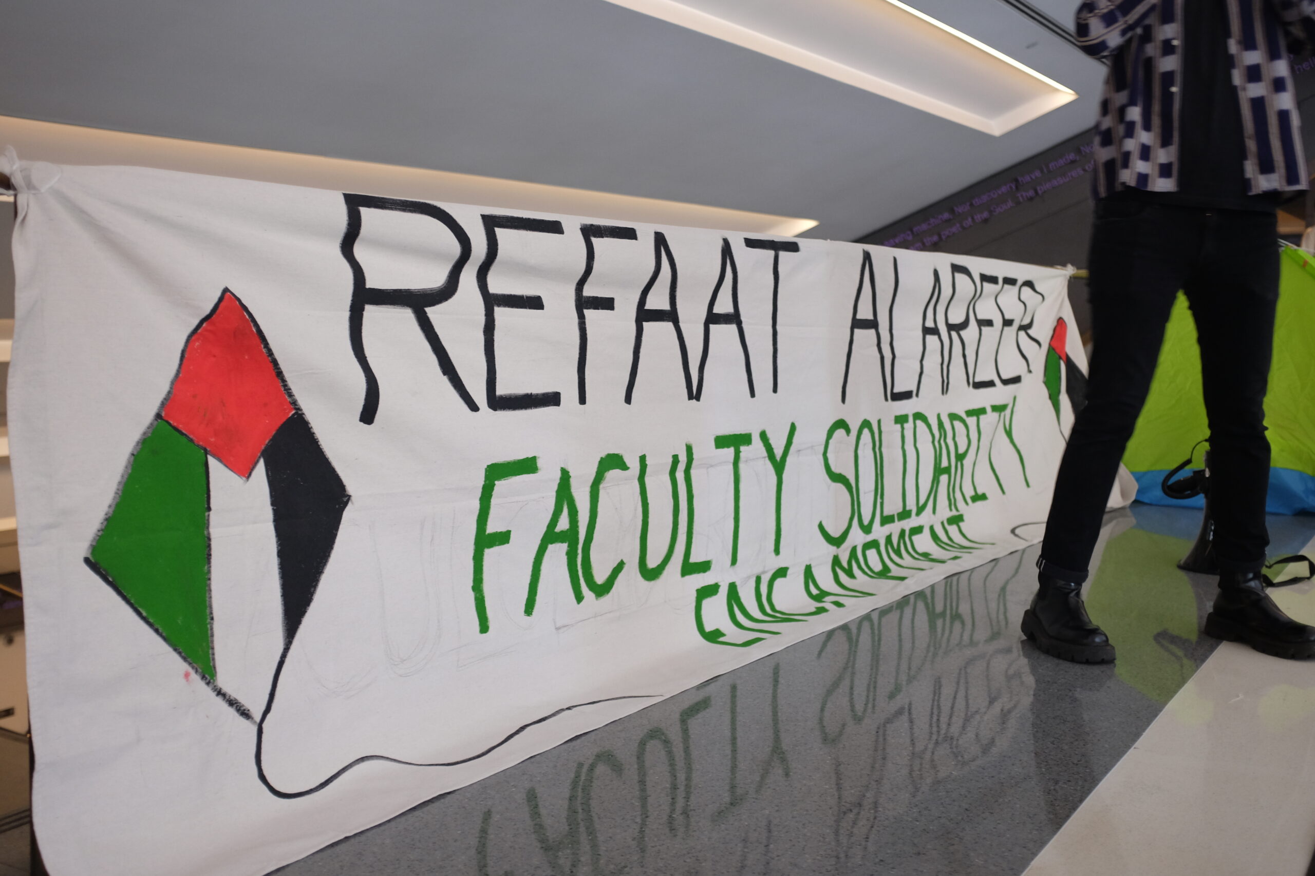 Photo of a banner that reads “Refaat Alareer Faculty Solidarity Encampment”. Next to the text are palestinian flags