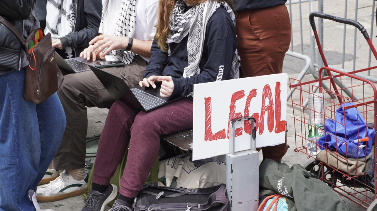 two people outside on computers sitting to the left of a sign that says "legal"