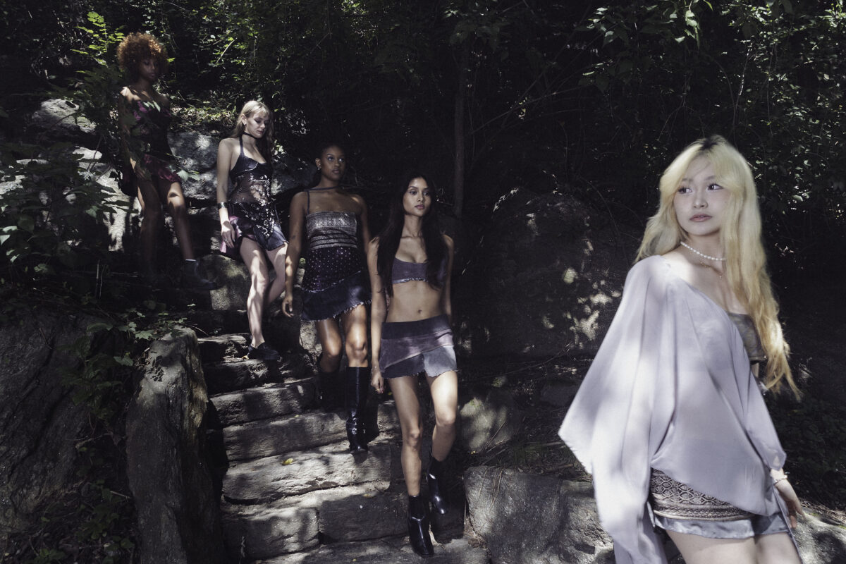 Group of models walking down stone steps in a forest, wearing intricate, layered outfits.