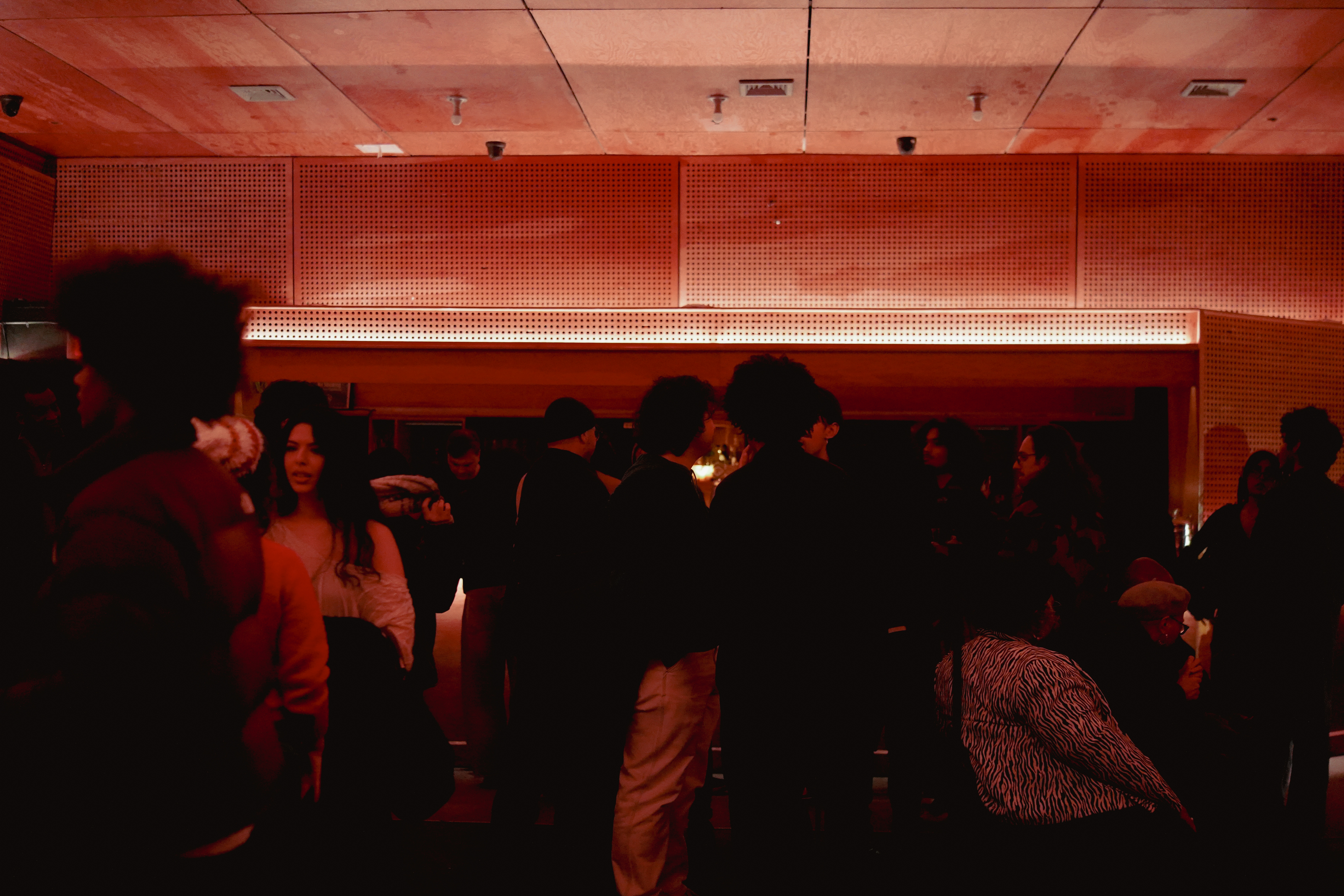 A dimly lit room with a crowd of people socializing under warm red lighting.
