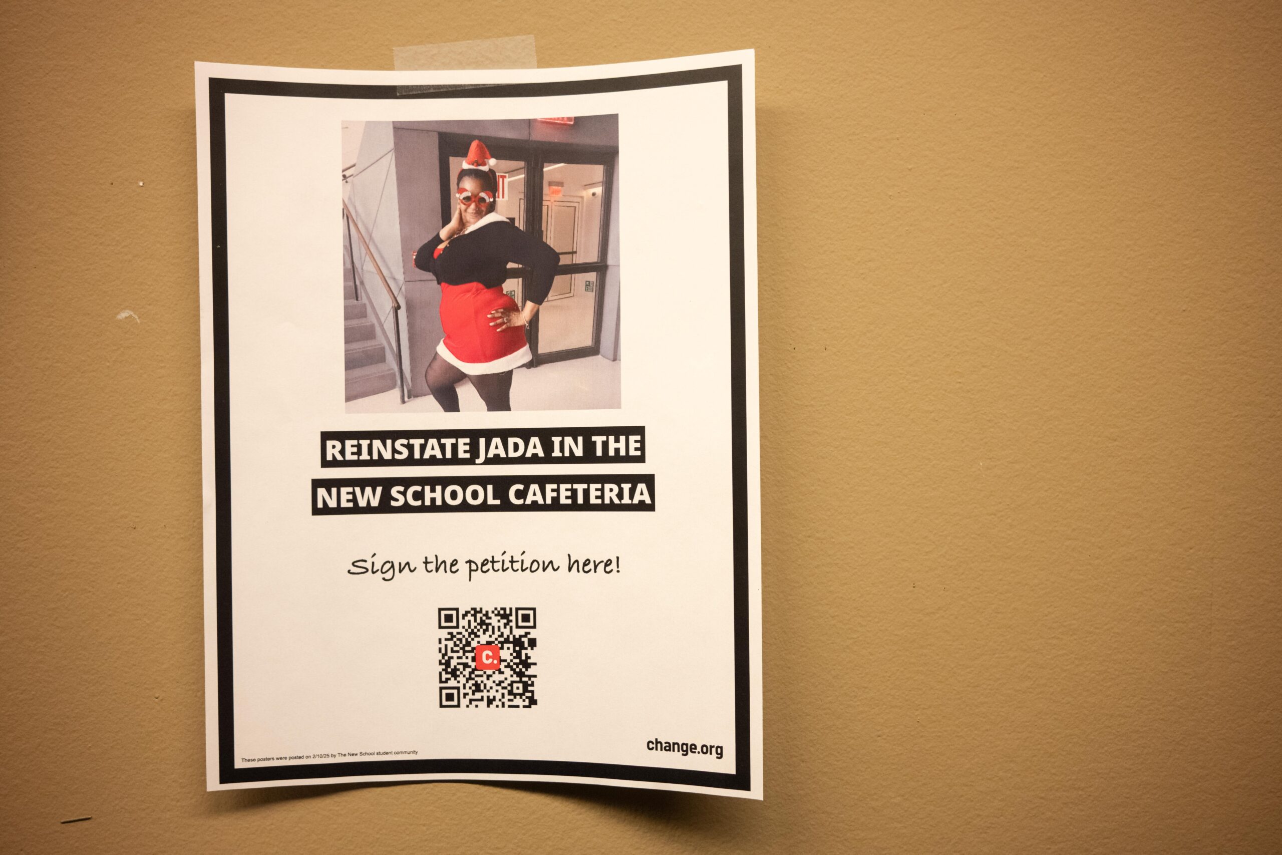 A petition flyer for reinstating Jada Graham in the UC Dining hall wall. The poster reads “REINSTATE JADA IN THE NEW SCHOOL CAFETERIA, Sign the petition here!” with a QR code below the words. Above the words shows a picture of Jada in a Christmas outfit. Photo of petition flyer by Dove Williams.