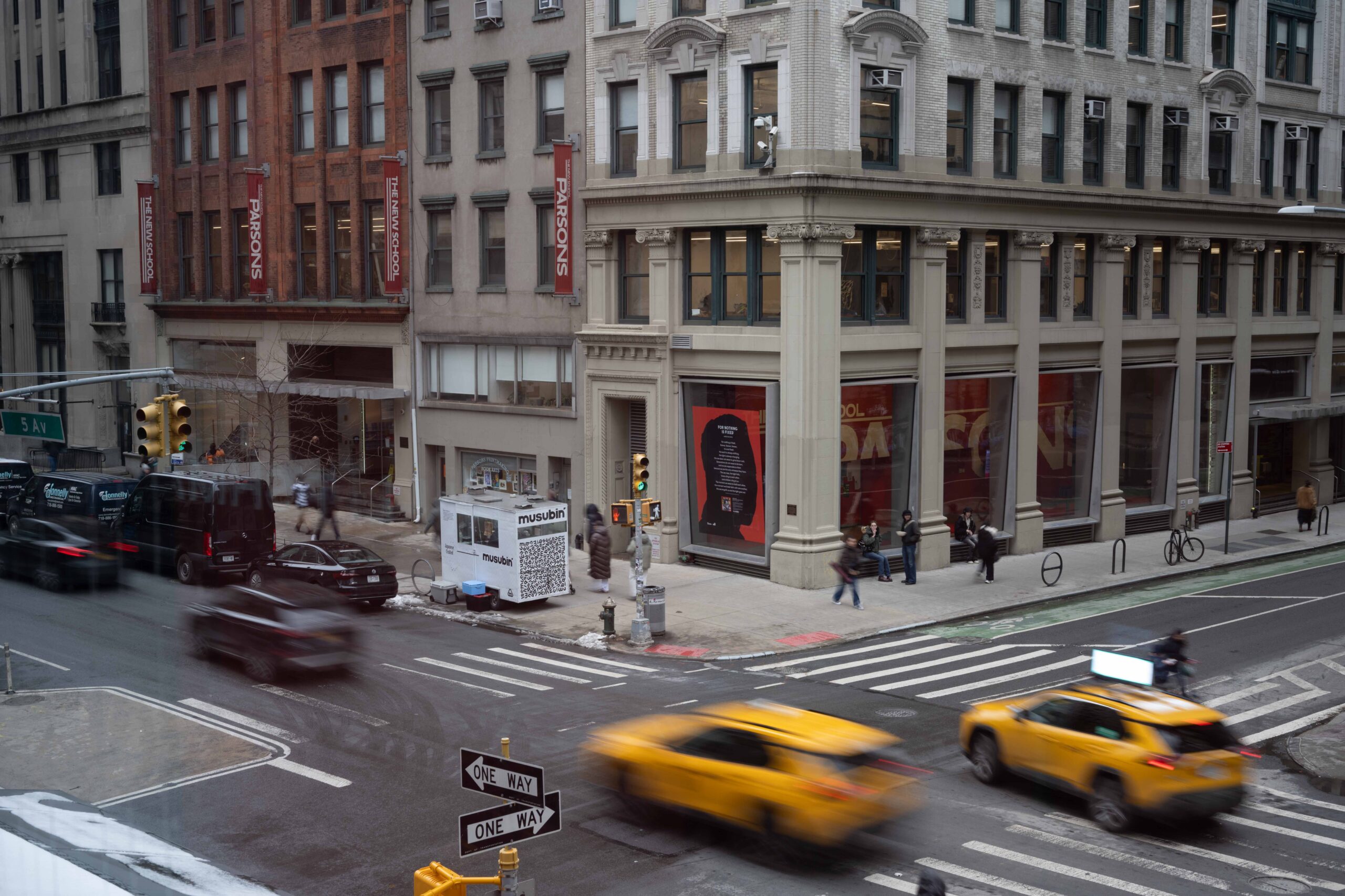 Wide shot of the Parsons building on the corner of 5th Avenue and 13th St. Taxi cabs and cars appear blurry as they drive down the avenue. Photo by Dove Williams