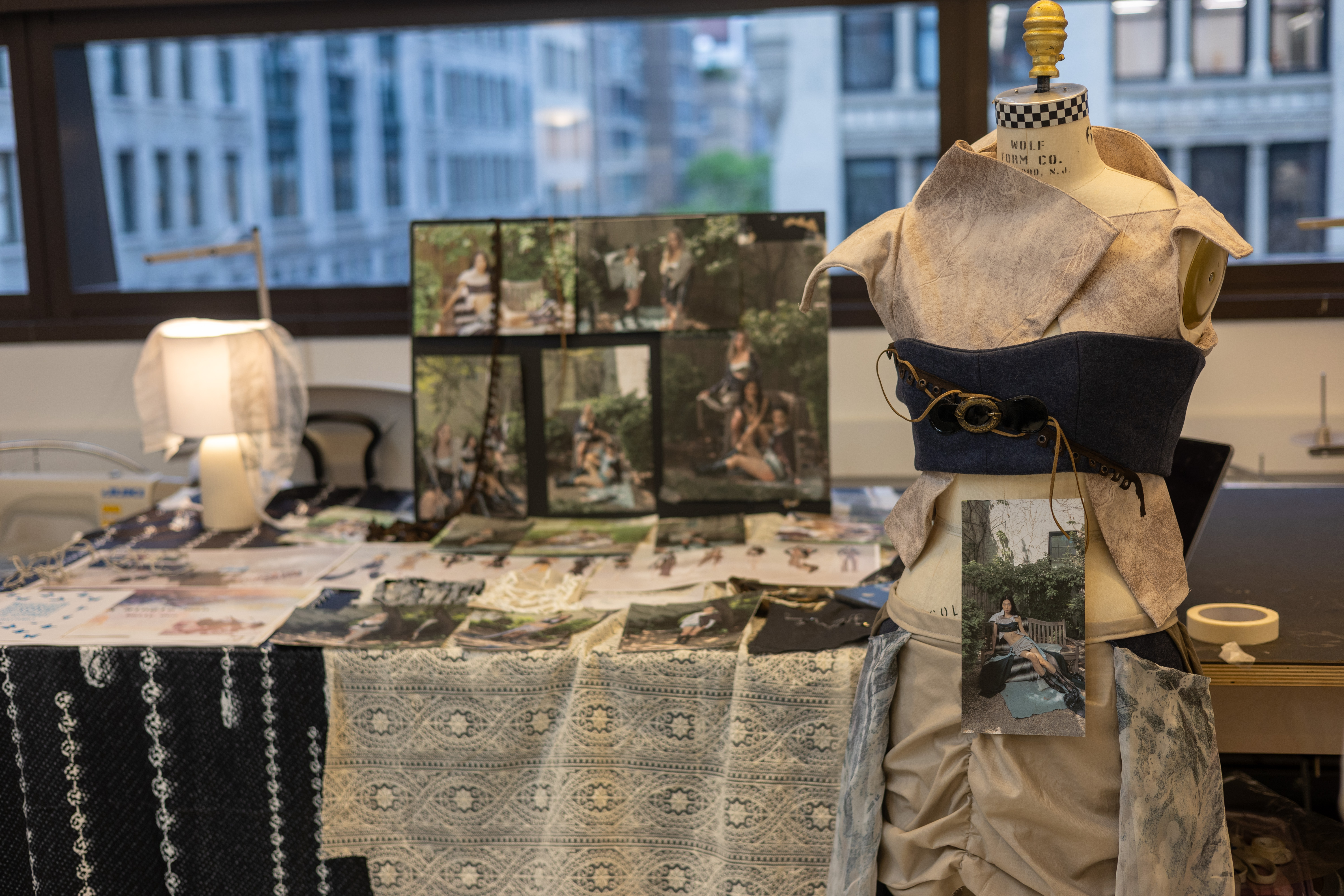 A mannequin at the front is dressed in layered white and black fabric. Photographs of a model are incorporated into the design of the dress and displayed on the back table behind it