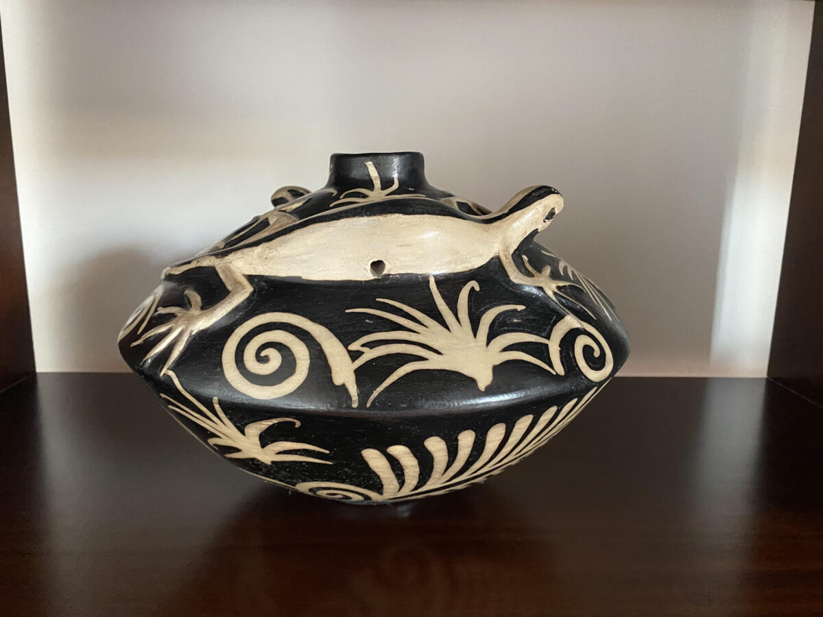 A black pot decorated with white designs and a white lizard on the top.