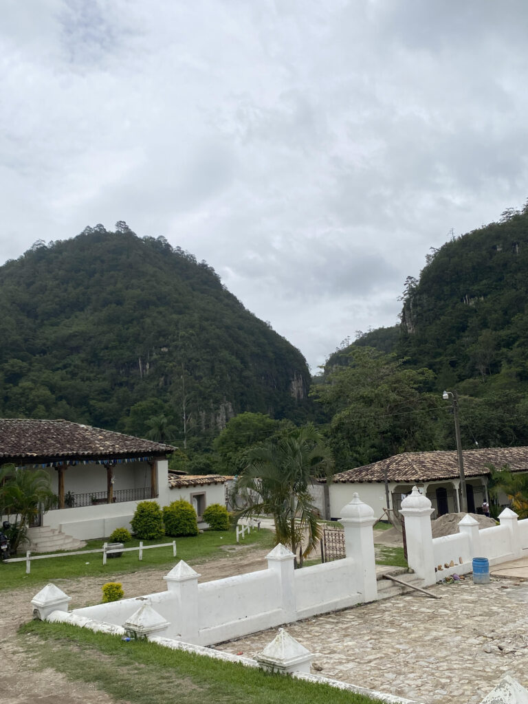 A village with white buildings and green mountains in the background.