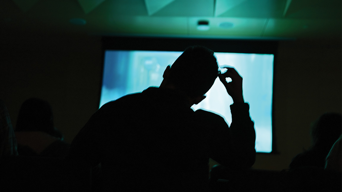 Silhouette of attendees against a bright, colorful screen.