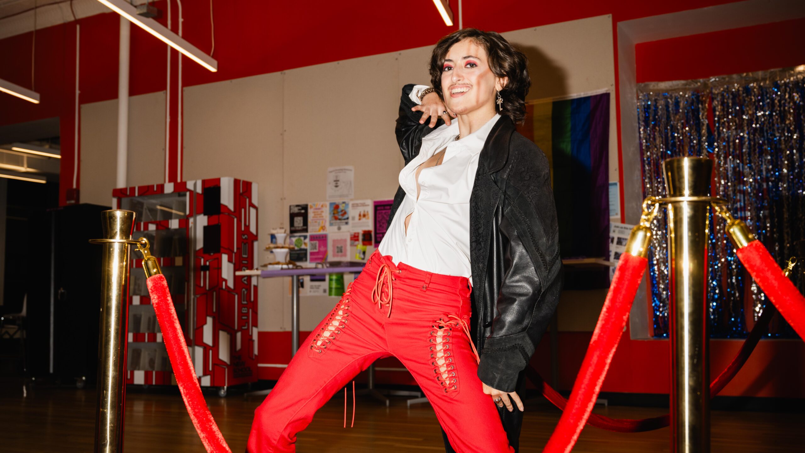 Spike, the drag performer for the night, dressed up in red pants, a white button down, and black trench coat lip-syncing on the runway.