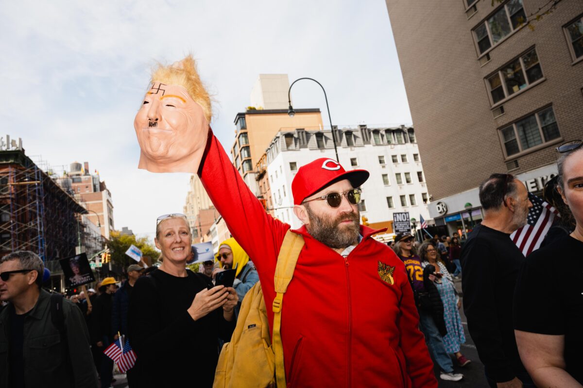 A man holds a decapitated Trump mask that wears Hitler’s mustache.