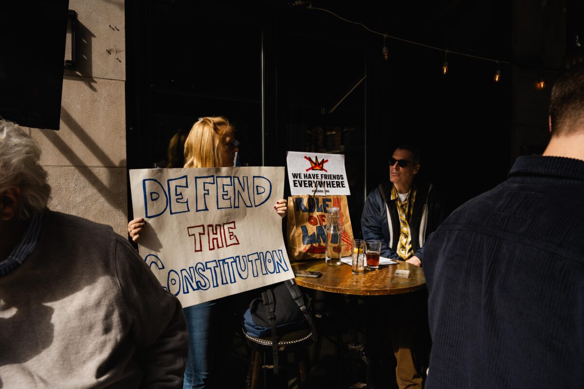 A couple with a “DEFEND THE CONSTITUTION” sign sits at a restaurant.
