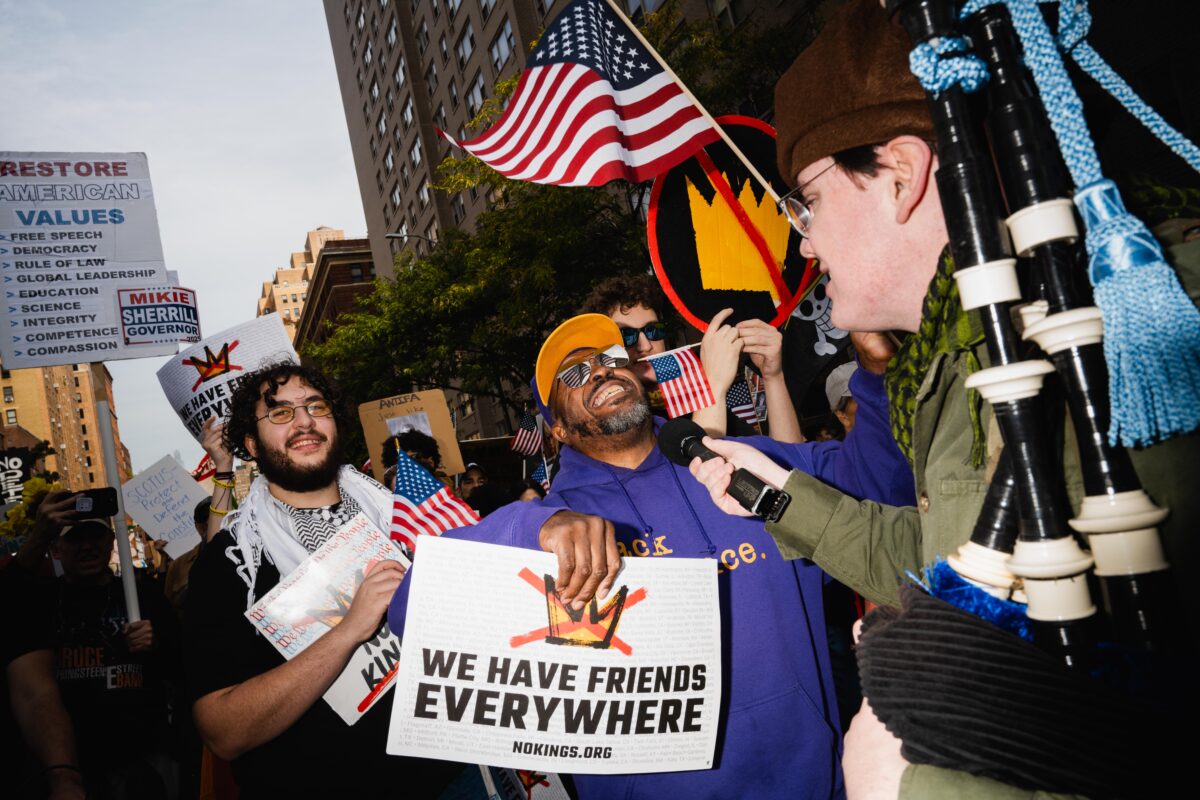 Man in purple sweatshirt speaking into a microphone at a protest.