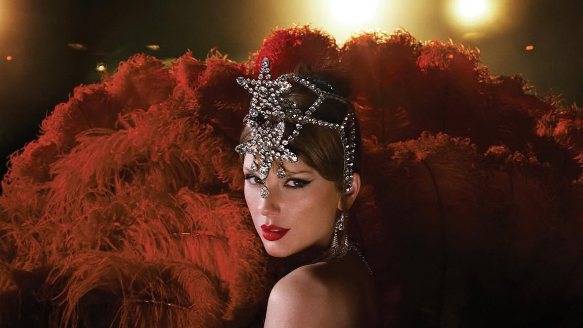 Image of Taylor Swift in a star-shaped bejeweled headband on a red feathered background.