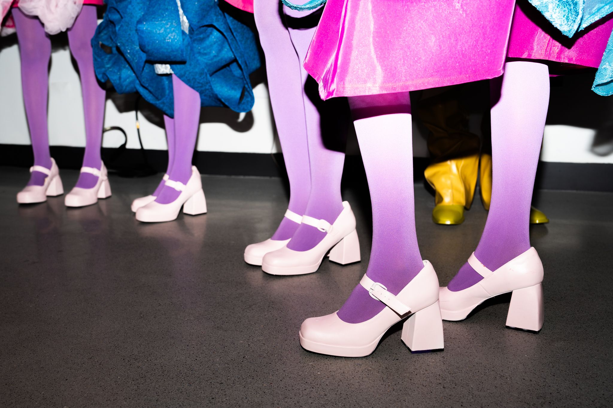 Close-up of pale pink platform Mary Jane shoes paired with purple tights on models standing in formation.