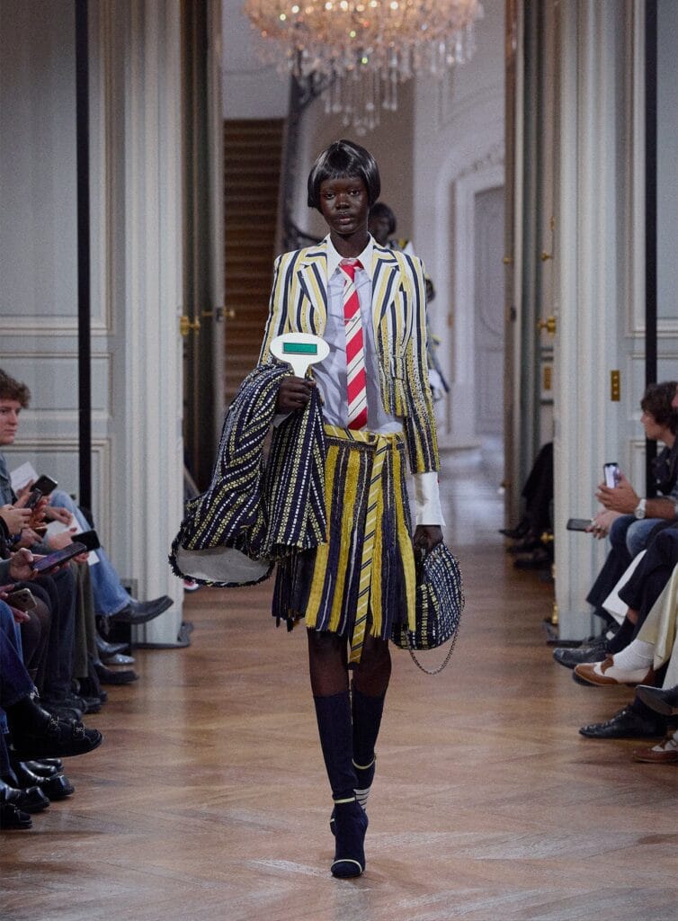 A model walks the runway in a striped, tailored suit with layered textures.
