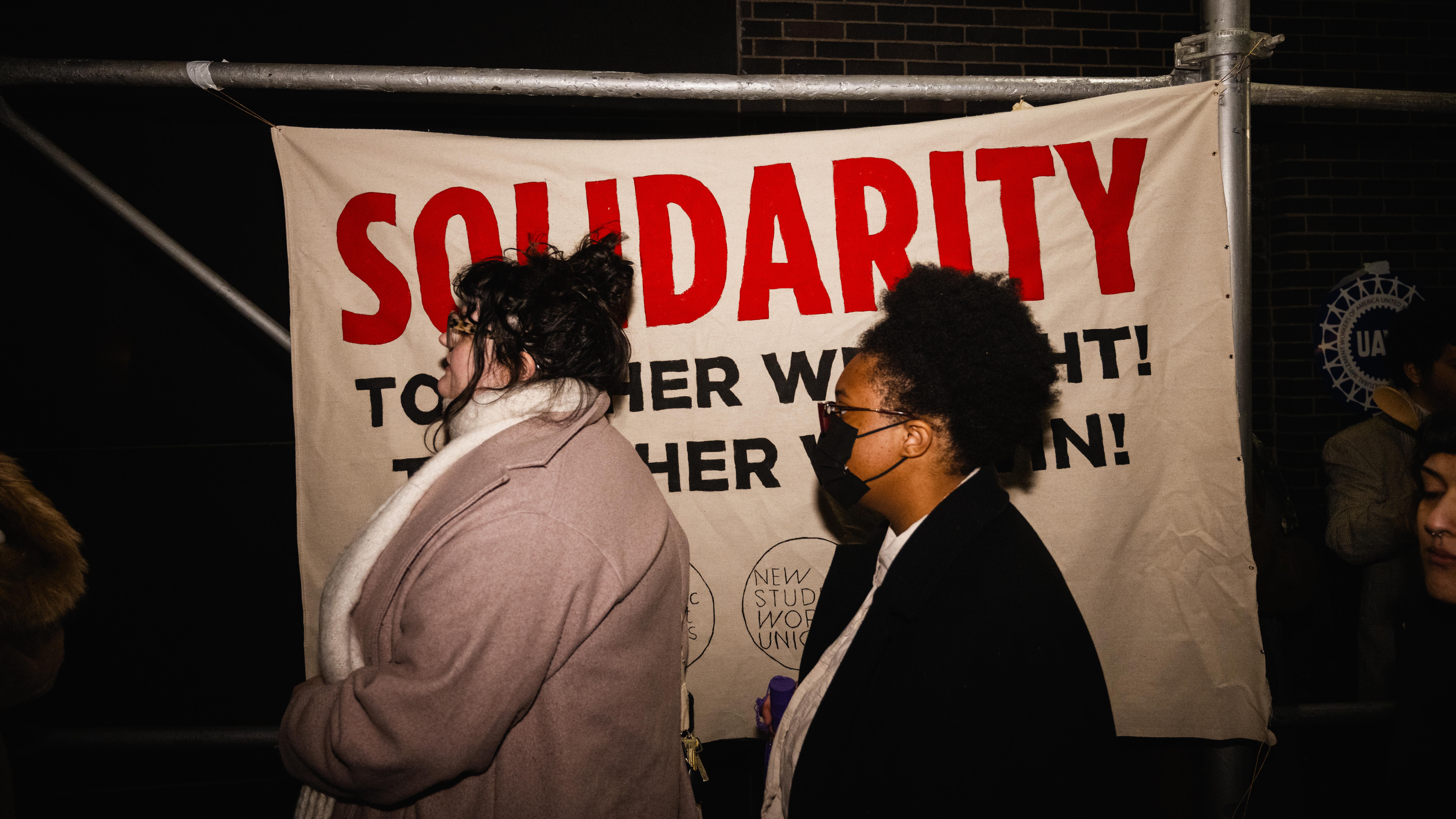 Two people walking in front of a sign that says “SOLIDARITY” in bold letters.