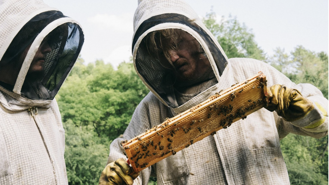 An image of the characters Teddy and Don inspecting a honeycomb from their apiary, from the film Bugonia.