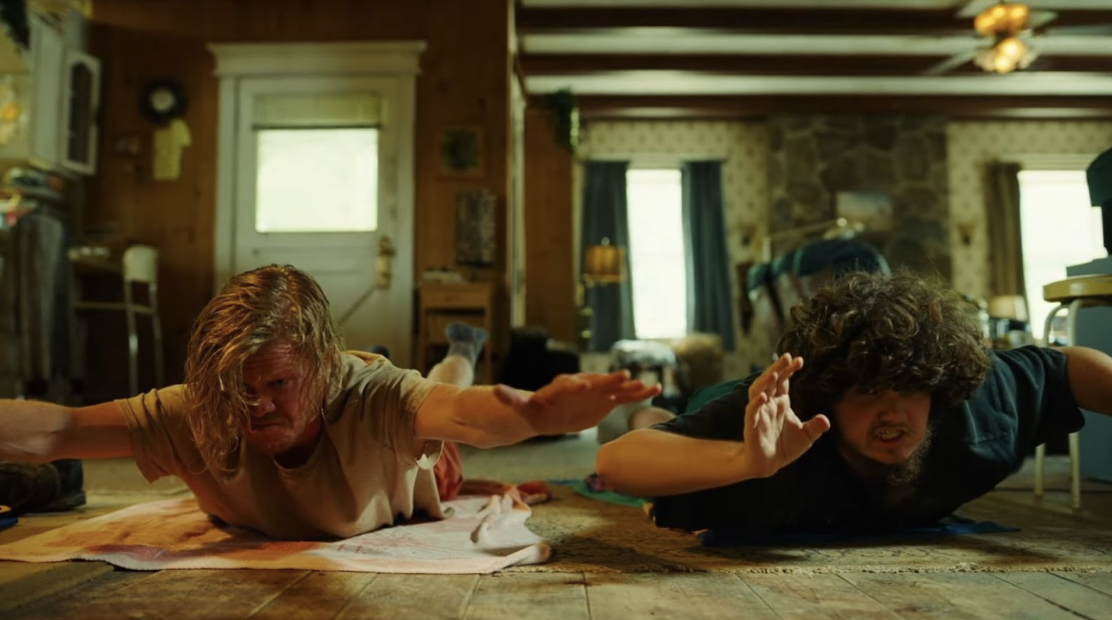 An image of Teddy and Don stretching out on beach towels from the film Bugonia.