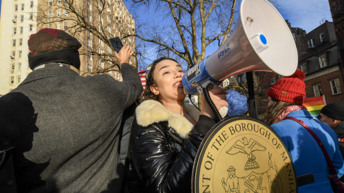 SLUG_MR_260216_0002_Angelica-Christina-addressing-crowd A woman speaking into a megaphone behind a podium with a plaque that says “President of the Borough of Manhattan.”