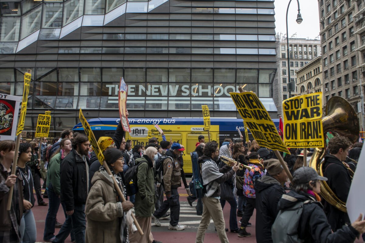 Protesters hold yellow signs reading “Stop the War on Iran” and “No New US War in the Middle East” in front of the 63 Fifth Ave. University Center.