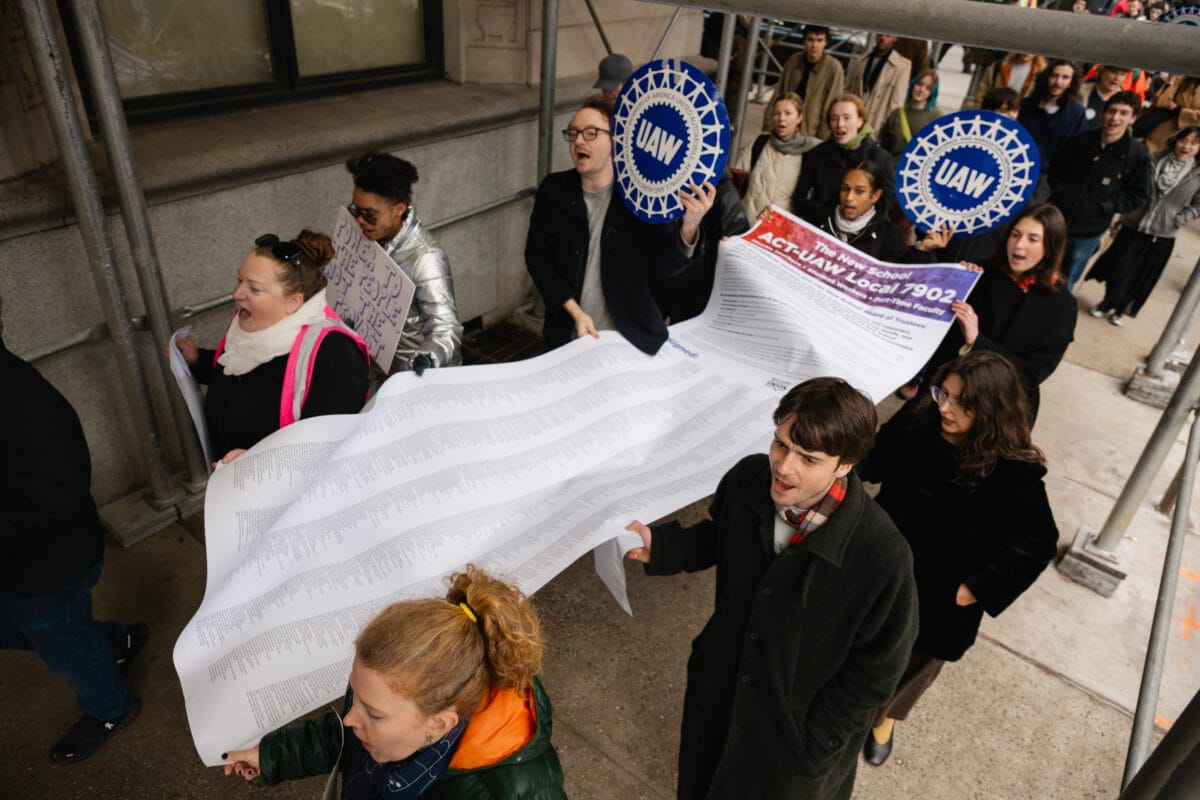 Students and faculty carry a large white letter down a sidewalk.