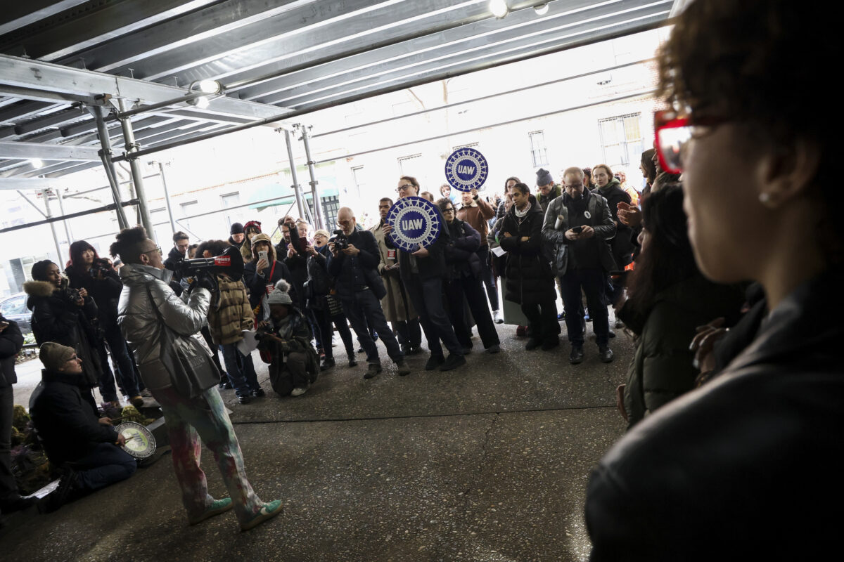 A crowd of faculty and students gather around a speaker holding a megaphone.