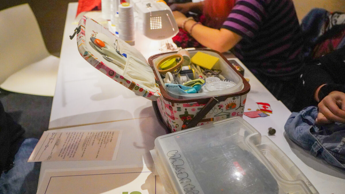 One student volunteers sewing kit sitting among other volunteers repair equipment.