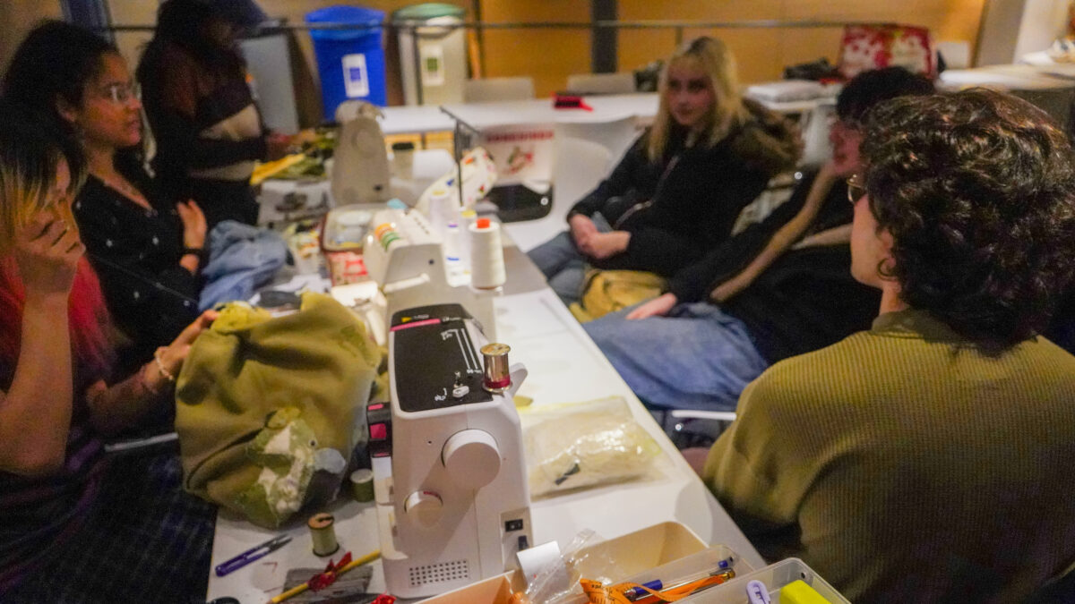 Attendees and student volunteers sitting and talking at the sewing table at the Repair Café.