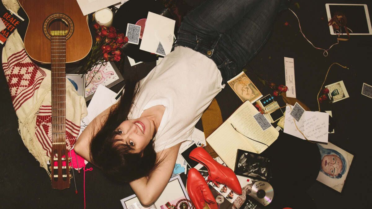 Elizabeth & the Catapult lays on the ground surrounded by an acoustic guitar and a scattering of objects that include papers, photos, red shoes, cds, artwork, flowers.