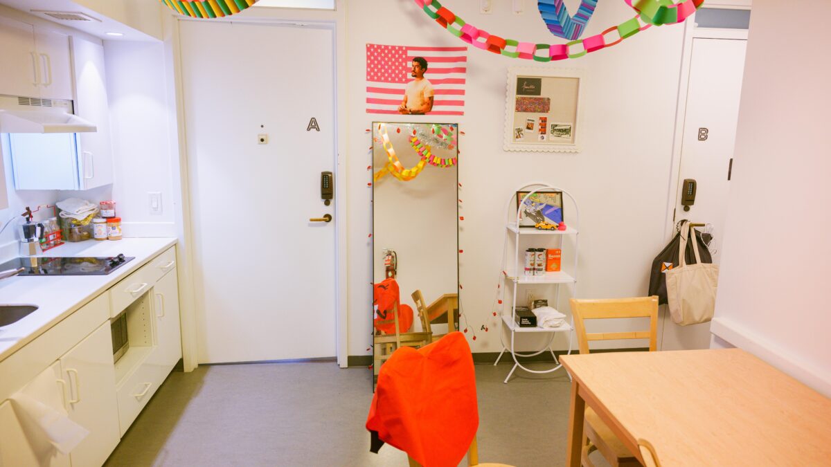 A furnished and decorated dormitory suite common space with a table, chairs, and kitchenette. 