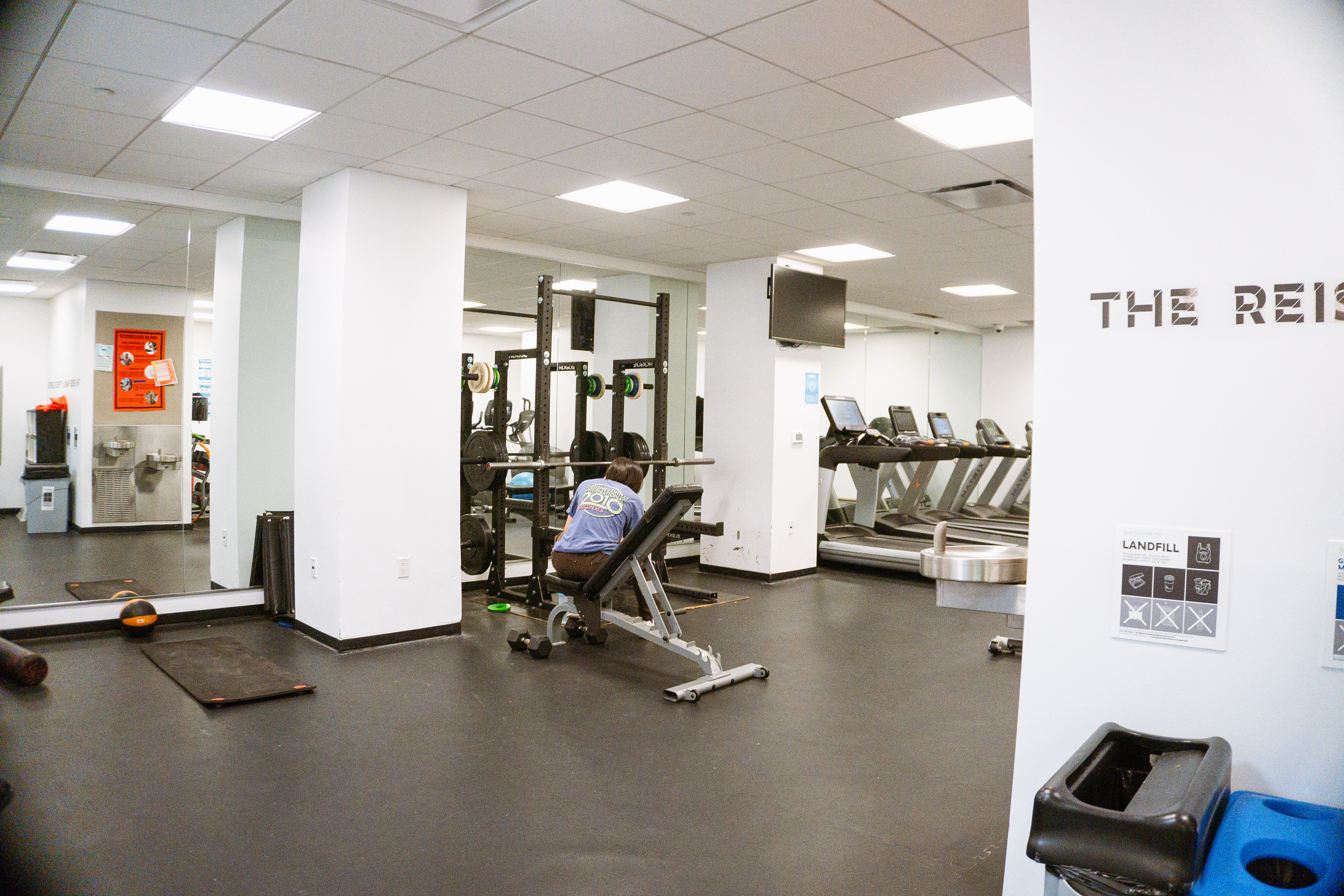 A small exercise room with treadmills, a bench, a yoga mat, a wall-mounted television, and floor-to-ceiling wall mirrors. 