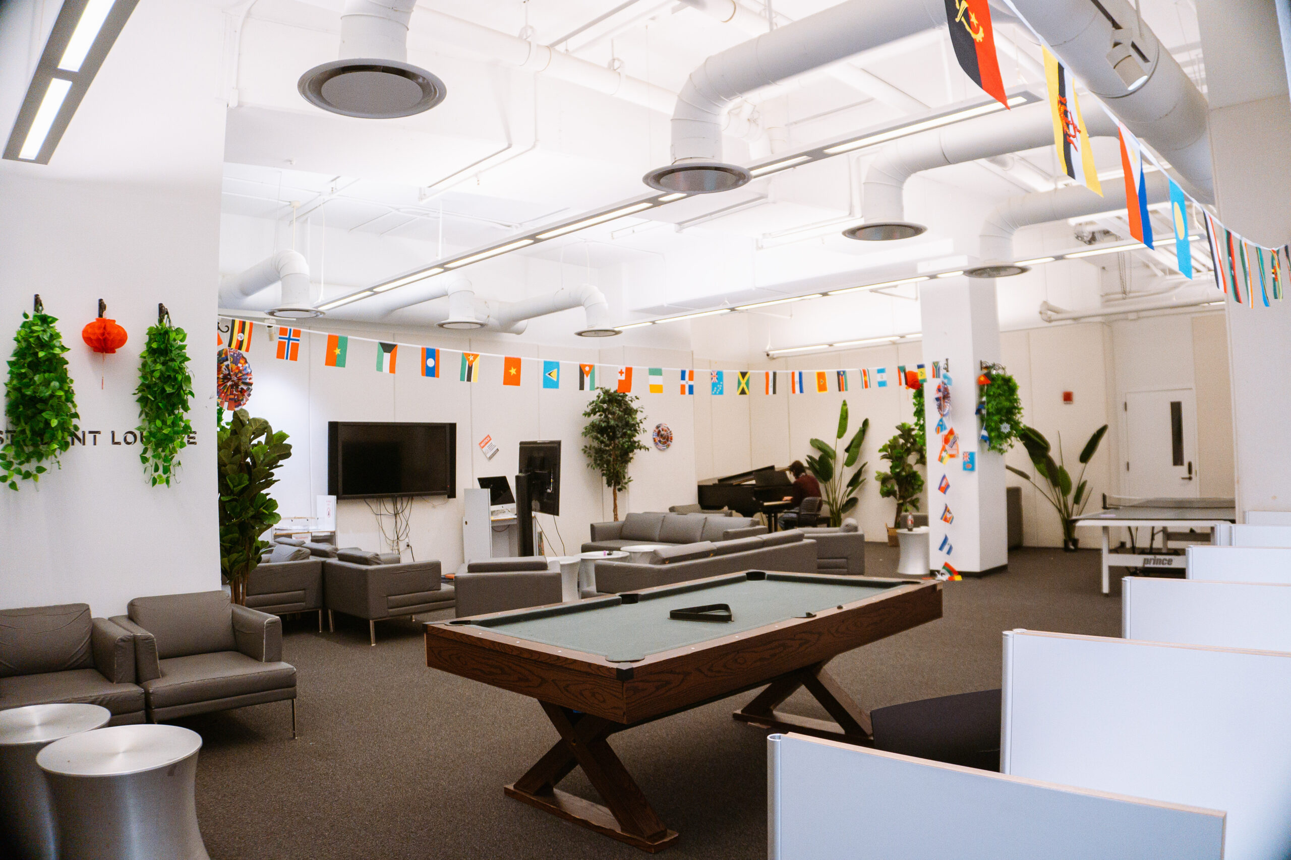 A large indoor lounge area with a pool table, ping pong table, wall-mounted television, couches, and chairs. 
