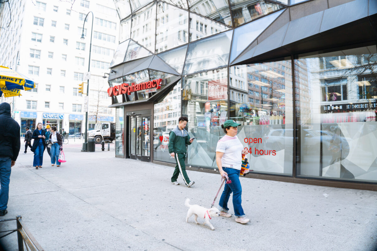 The corner of a large gray geometric building with big windows and automatic sliding doors under a sign that reads “CVS Pharmacy.”
