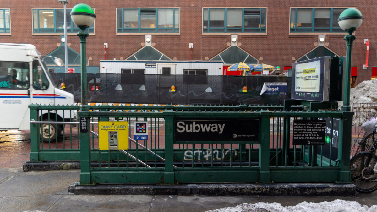 A subway entrance across the street from a brick building.
